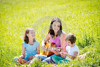 Mother playing guitar in nature to children