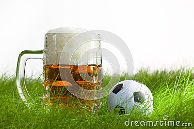 Mug of beer and soccer ball on grass