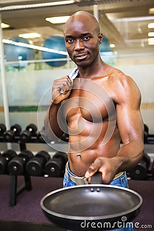 Muscular man holding frying pan in gym