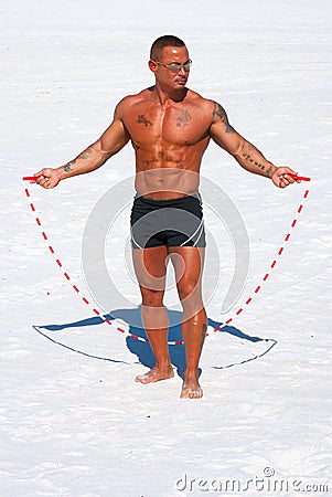 Muscular man with jump rope on the beach