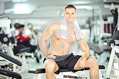 Muscular young guy sitting on a bench in a gym