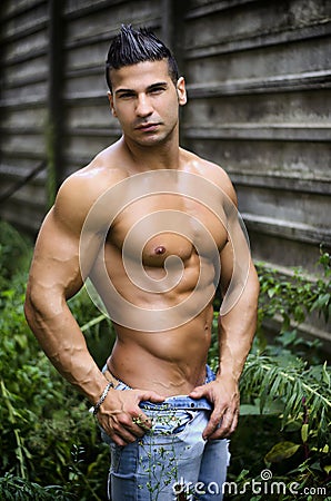 Muscular young latino man shirtless in jeans in front of concrete wall