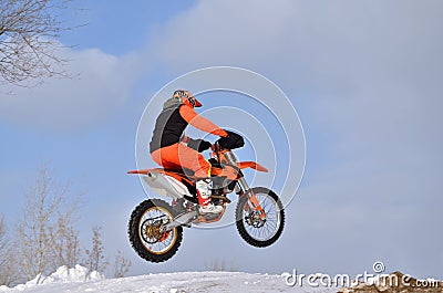 MX rider on the bike jumps from a hill on a snowy highway