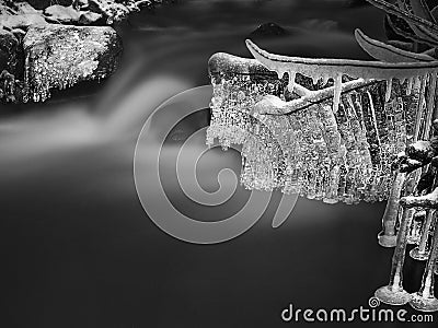 Night winter view to icicles on twigs and icy boulders above rapid stream. Reflections of head lamp in icicles. Black and white.