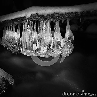 Night winter view to icicles on twigs and icy boulders above rapid stream. Reflections of head lamp in icicles. Black and white.