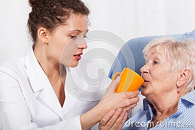 Nurse gives drinking old woman