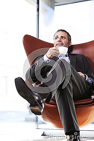 Office manager in red chair enjoying coffee.