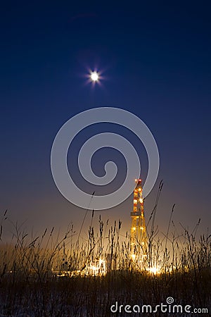 Oil well in the snowy landscape lit up at night.