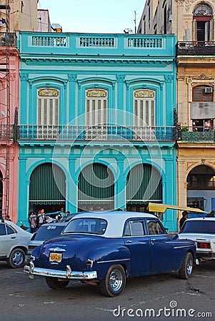 Old blue Plymouth car in front of colourful building in Cuba