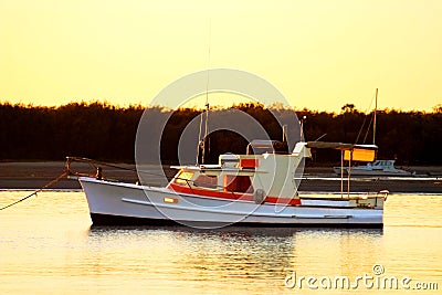 Old wooden motor boat sits still at anchor as the sun rises.