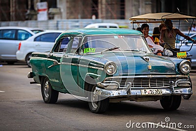 Old vintage classic taxi car driving on Cuban Havana city street with people in background