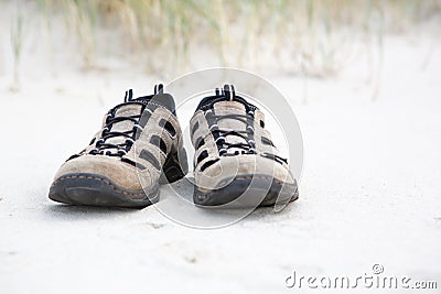 Old walking shoes on beach with white sand