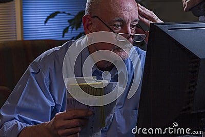 Older man looks worried as he pays bills online, horizontal