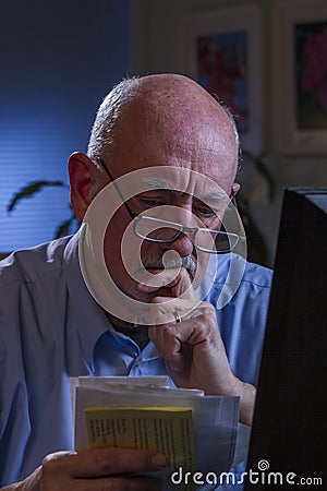 Older man looks worried as he pays bills online, vertical