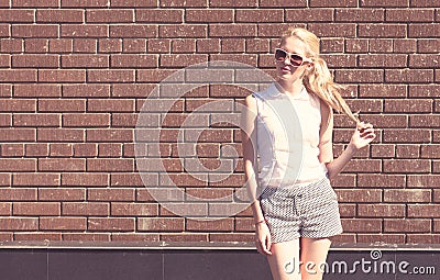 Outdoor summer sensual fashion portrait beautiful young blond woman and twisting hair near the brick wall background. Toned in war