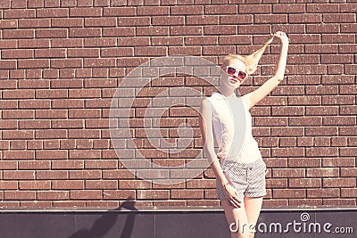 Outdoor summer sensual fashion portrait beautiful young blond woman and twisting hair near the brick wall background. Toned in war
