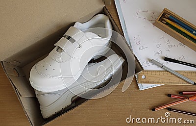 Pair of sneakers in shoe cardboard box on student table.