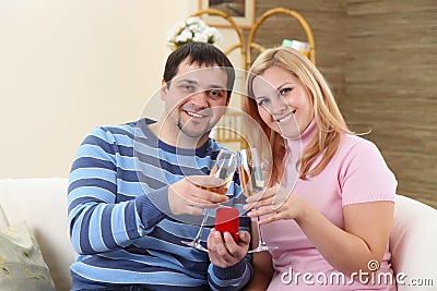 Pares enamorados jovenes con los vidrios de un champán y de un regalo