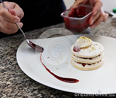 Pastry chef is decorating the dessert with berry sauce