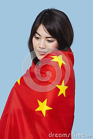 Patriotic young woman wrapped in Chinese flag over blue background