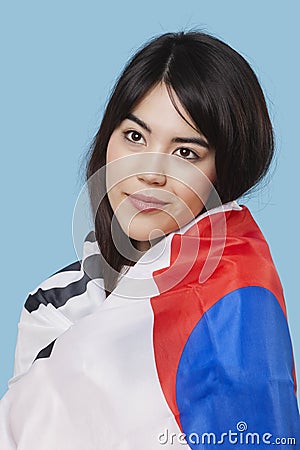 Patriotic young woman wrapped in Korean flag over blue background