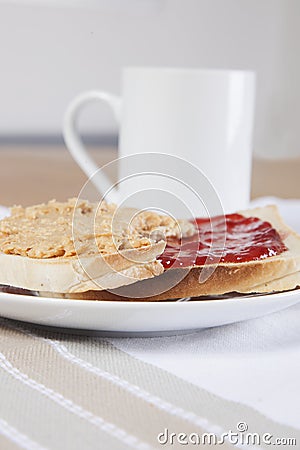 Peanut butter and jam on slices of bread with cup of coffee