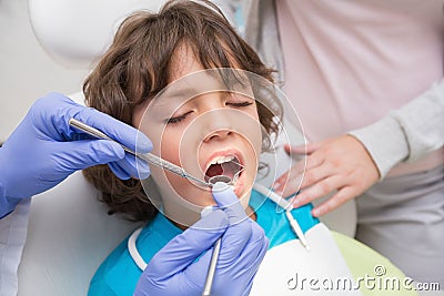 Pediatric dentist examining a little boys teeth with his mother