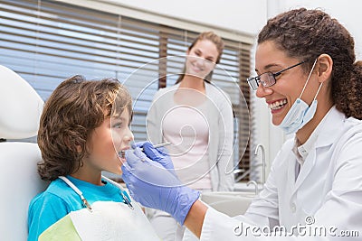 Pediatric dentist examining a little boys teeth with his mother watching