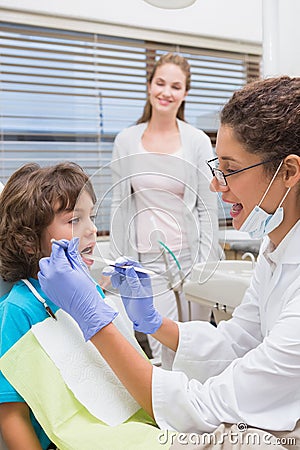 Pediatric dentist examining a little boys teeth with his mother watching