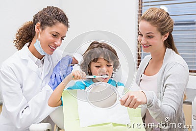 Pediatric dentist showing little boy how to brush teeth with his mother