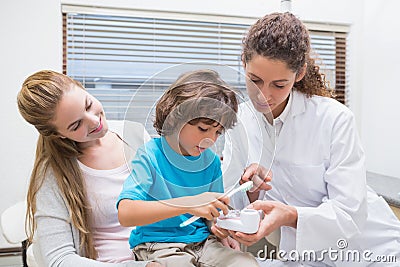 Pediatric dentist showing little boy how to brush teeth with his mother