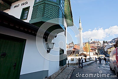 People and cars move on the narrow street with mosque and old Ottoman style house