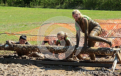 People Jumping over muddy logs in the Mud while competing in a Mud Run