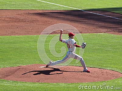 Philles Cole Hamels steps forward to throw pitch with arm in the air and shadow casting on the ground