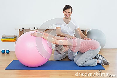 Physical therapist assisting senior woman with yoga ball