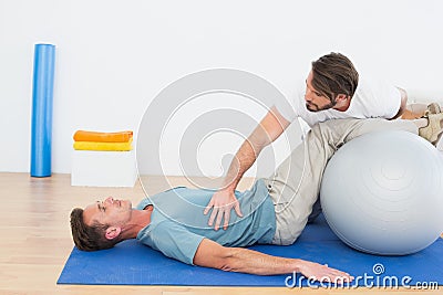 Physical therapist assisting young man with yoga ball
