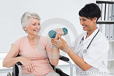 Physiotherapist assisting senior woman to lift dumbbell