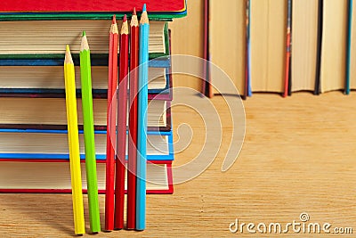 Pile of books and colored pencils on a wooden surface.