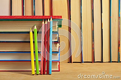 Pile of books and colored pencils on a wooden surface.