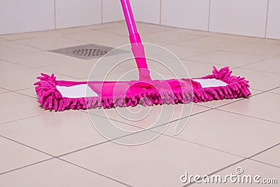 Pink mop cleaning tile floor in bathroom