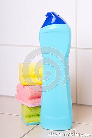 Plastic bottle of cleaning product and three sponges on tiled fl