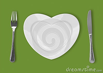 Plate in shape of heart, table knife and fork on green backgroun