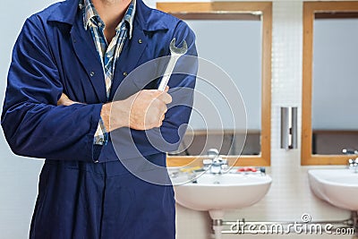 Plumber in blue boiler suit posing with wrench