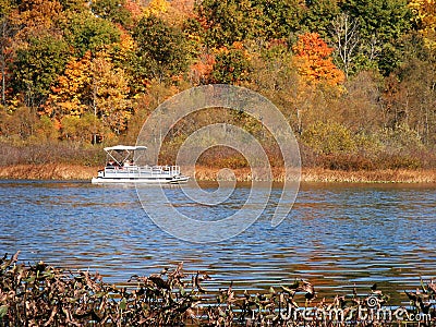 Pontoon boat on a lake with orange and green autumn trees. .