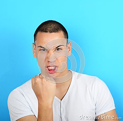 Portrait of angry man screaming showing fist against blue backgr