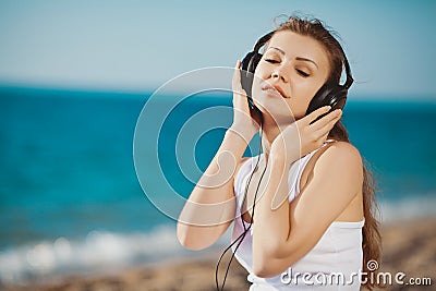 Portrait of beautiful woman sitting on the beach near the sea in headphones listening to music