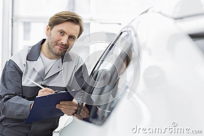 Portrait of confident automobile mechanic holding clipboard while leaning on car s window in workshop