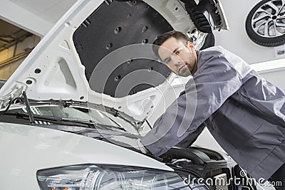 Portrait of confident male repair worker repairing car engine in repair shop