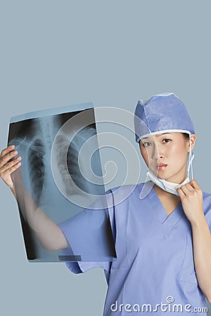 Portrait of a female surgeon holding x-ray report over light blue background