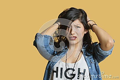 Portrait of a frustrated young woman with hands in hair over colored background